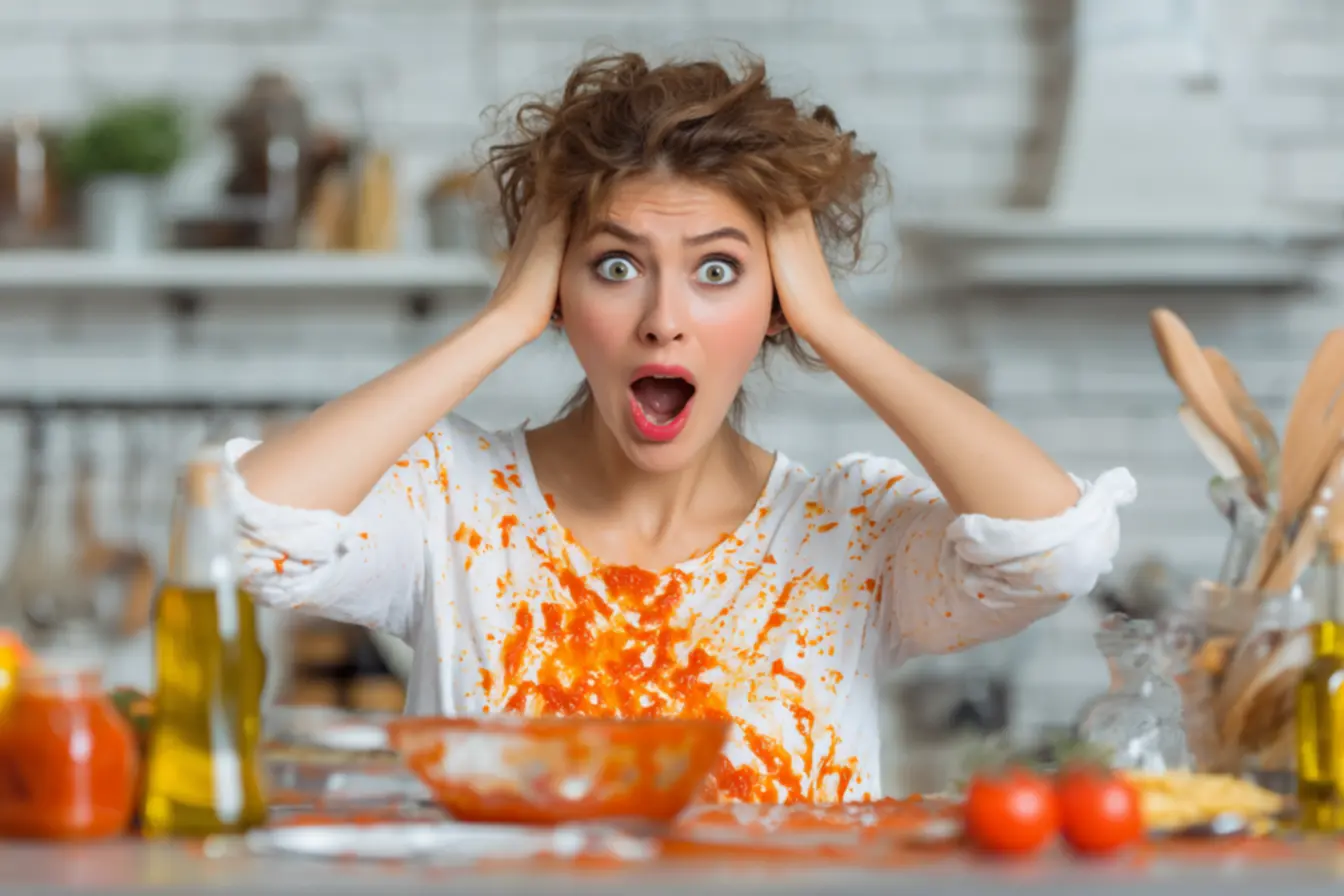 Mãos removendo delicadamente o excesso de molho de tomate de uma camiseta com papel toalha, focando na ação rápida para manchas em tecidos.