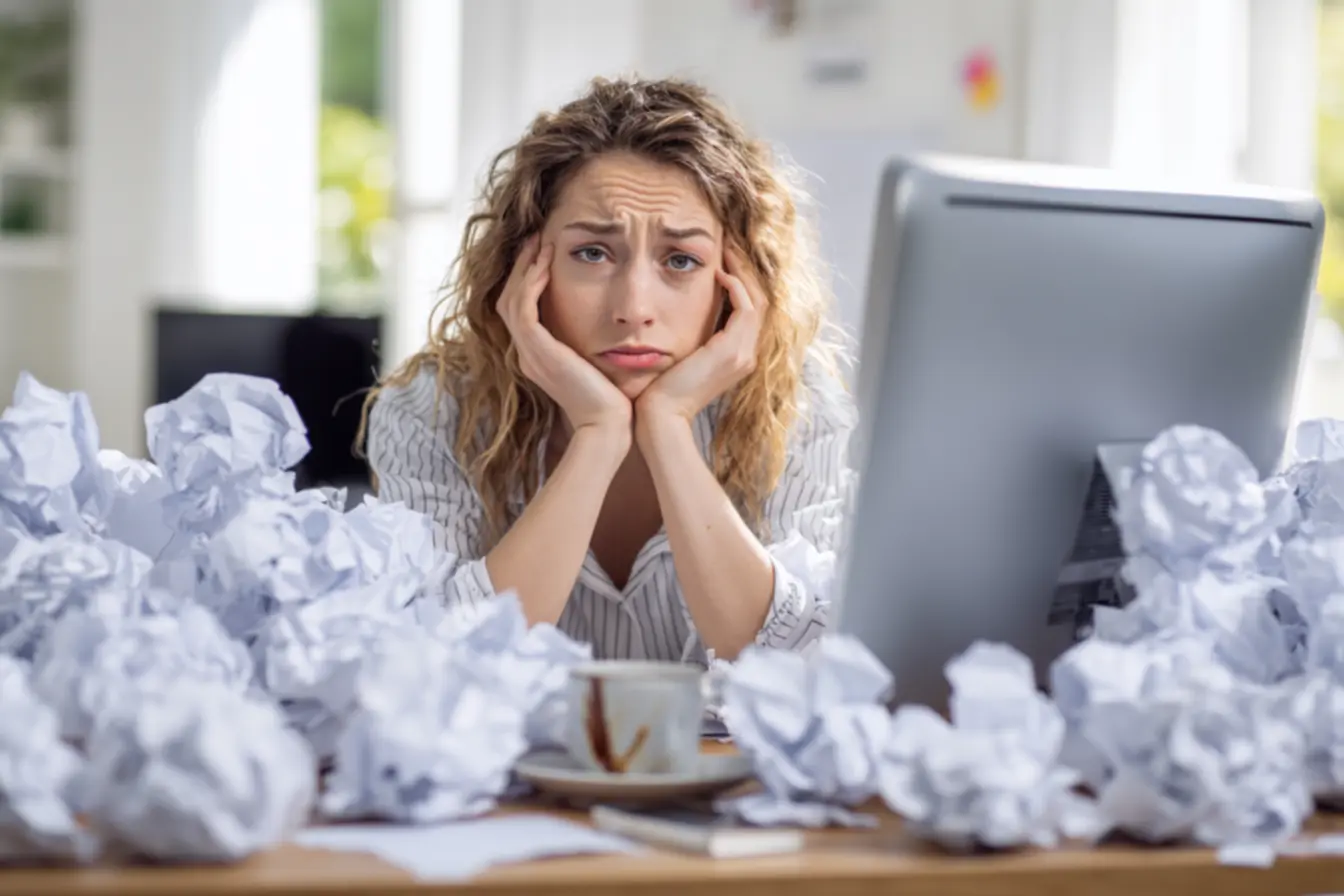 Mulher pensativa olhando para a tela do computador, refletindo sobre as interrupções no seu dia.